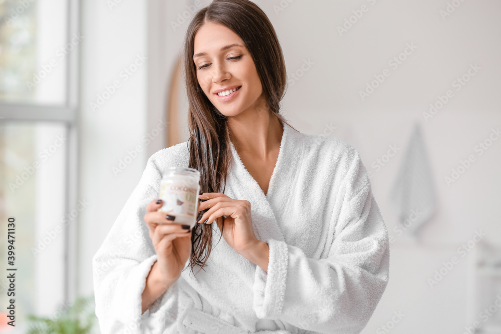 Beautiful young woman applying coconut oil on her hair in bathroom