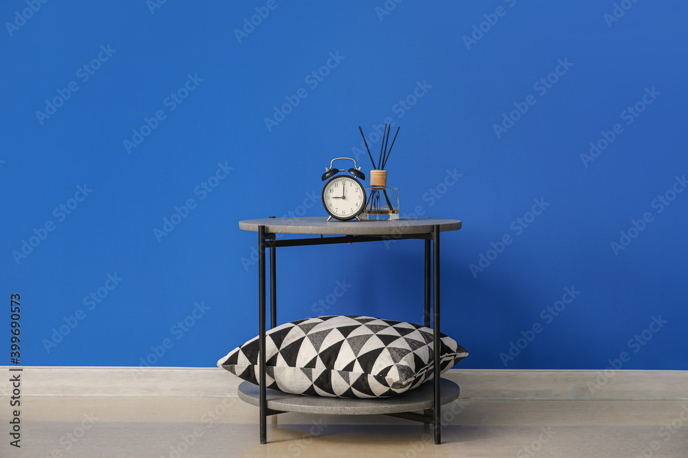 Stylish table with pillow and clock near color wall