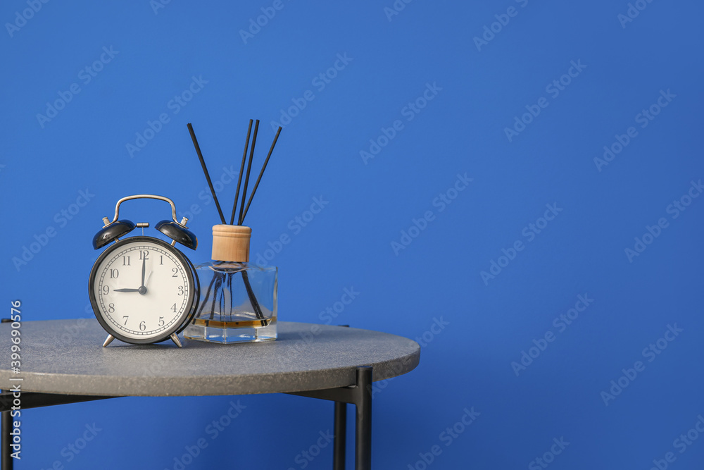 Stylish table with reed diffuser and clock near color wall