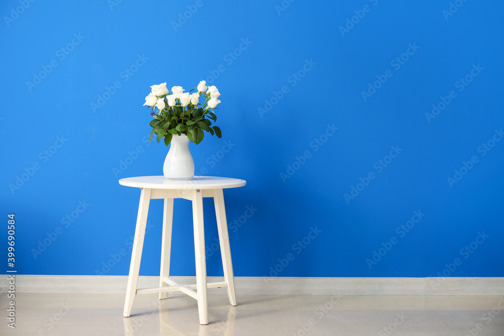 Beautiful vase with roses on table near color wall