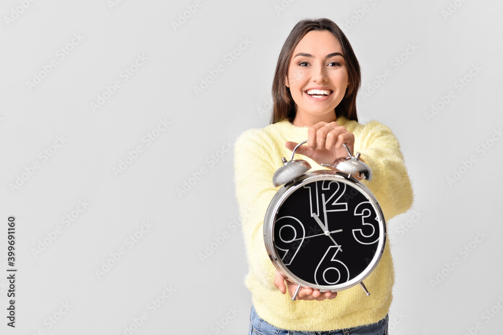 Beautiful young woman with alarm clock on grey background