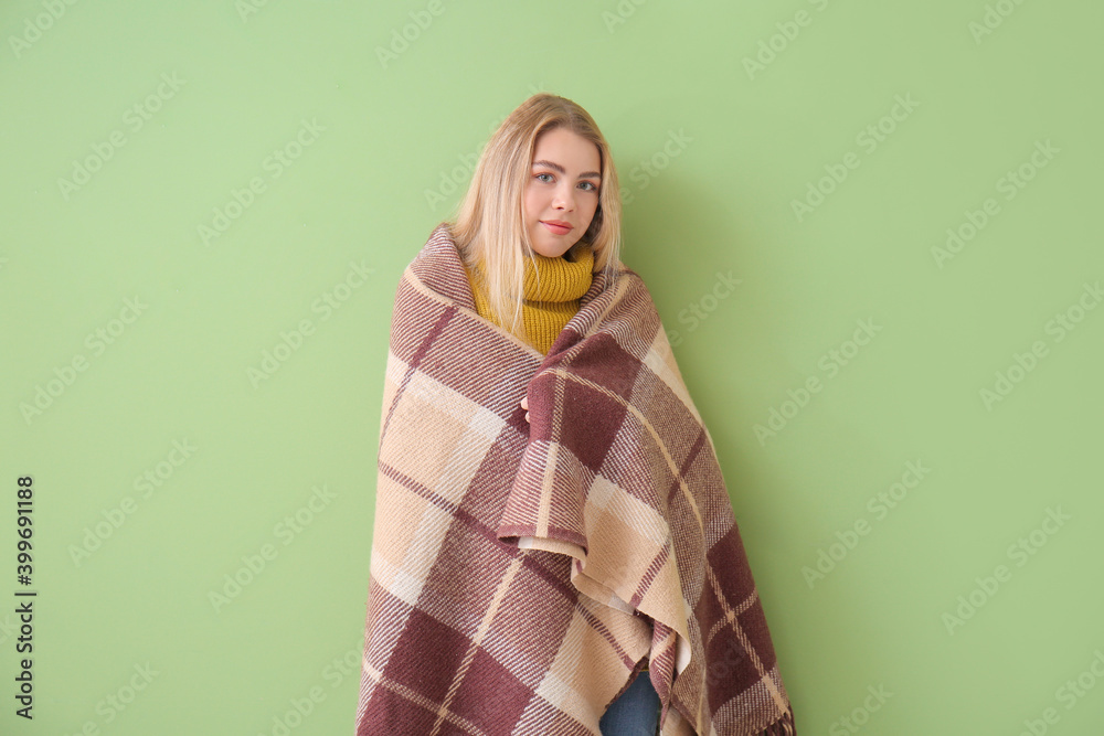 Young woman wrapped in warm plaid on color background. Concept of heating season