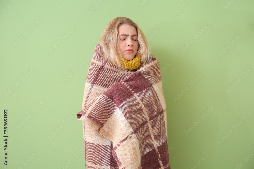 Young woman wrapped in warm plaid on color background. Concept of heating season