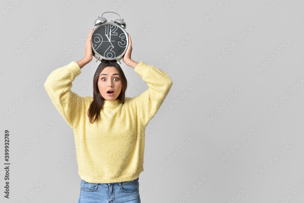 Stressed young woman with alarm clock on grey background