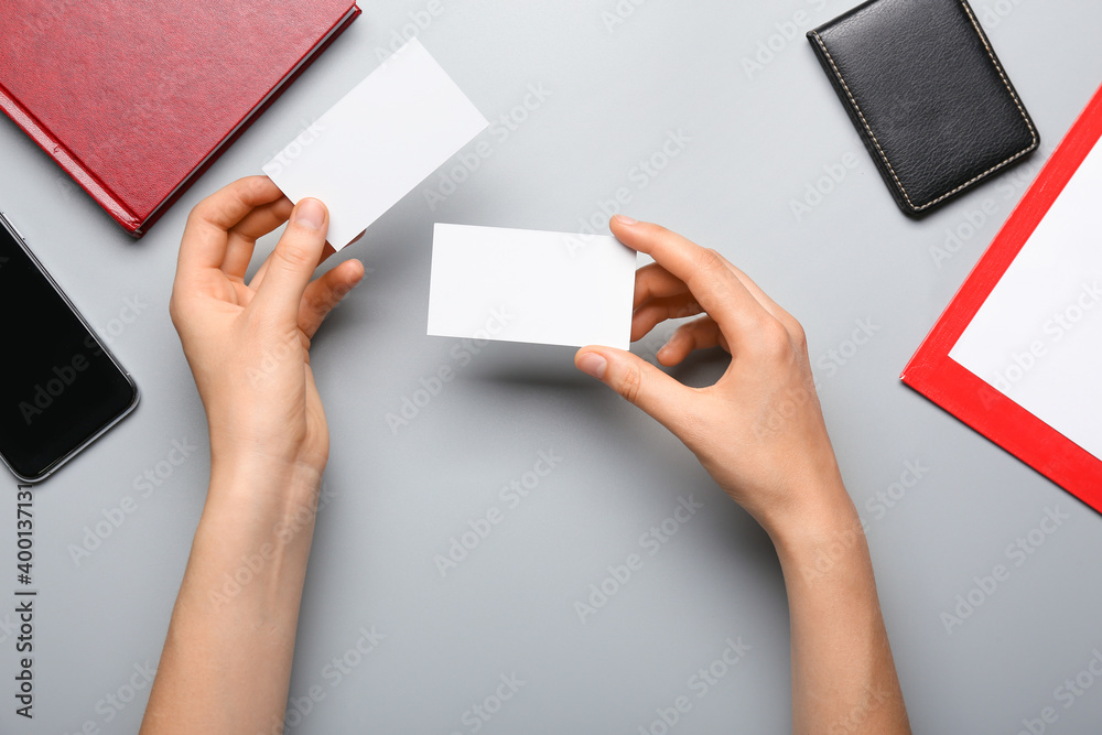 Hands with blank paper cards, mobile phone and stationery on gray background