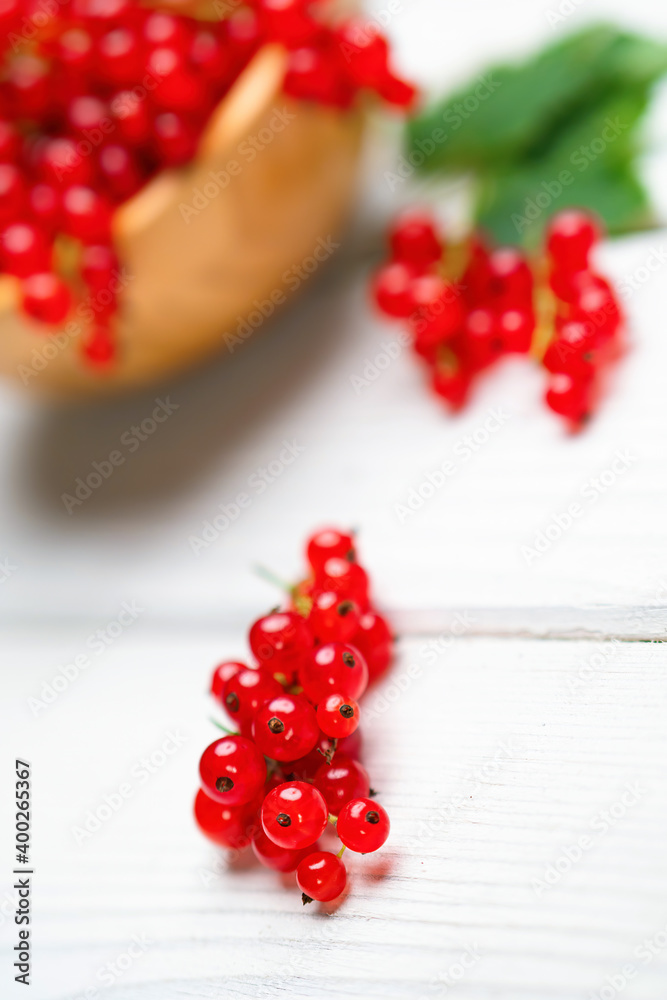 Fresh ripe red currant berries (Ribes rubrum) with leaves in bowl on white wooden table. Healthy org