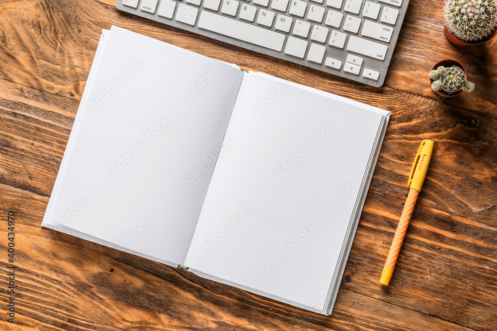 Composition with blank book and computer keyboard on wooden table