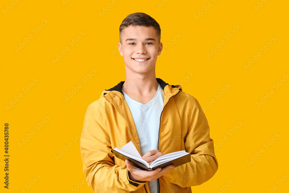 Teenage boy with book on color background