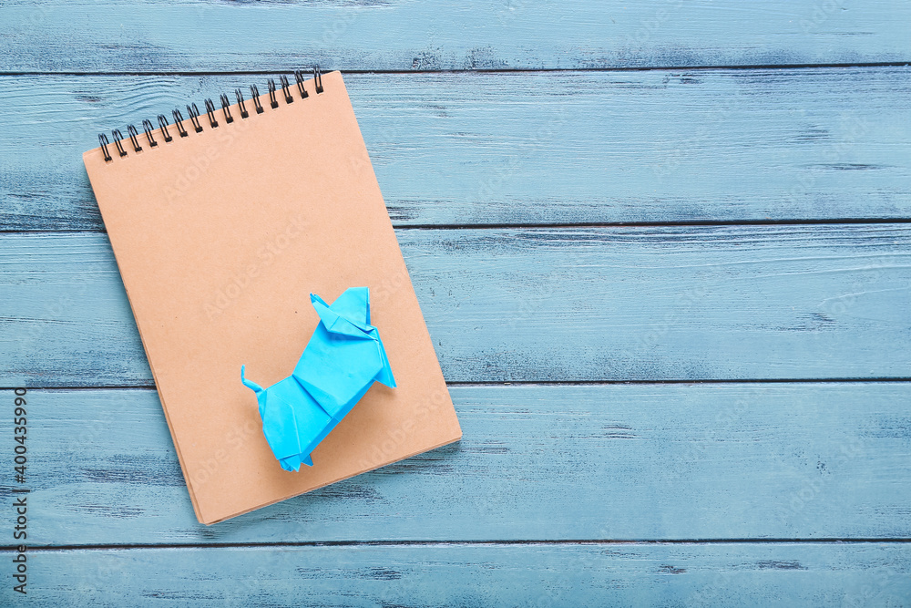 Notebook and origami bull as symbol of year 2021 on color wooden background