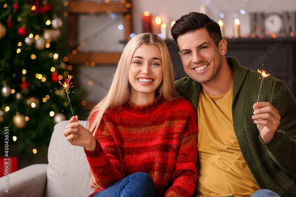 Happy young couple with sparklers celebrating Christmas at home