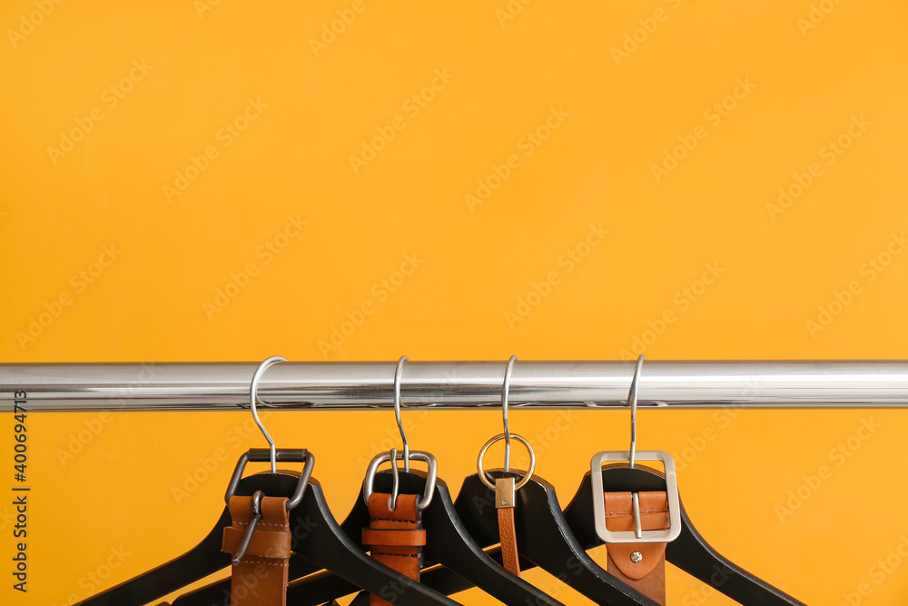 Rack with clothes hangers and belts on color background