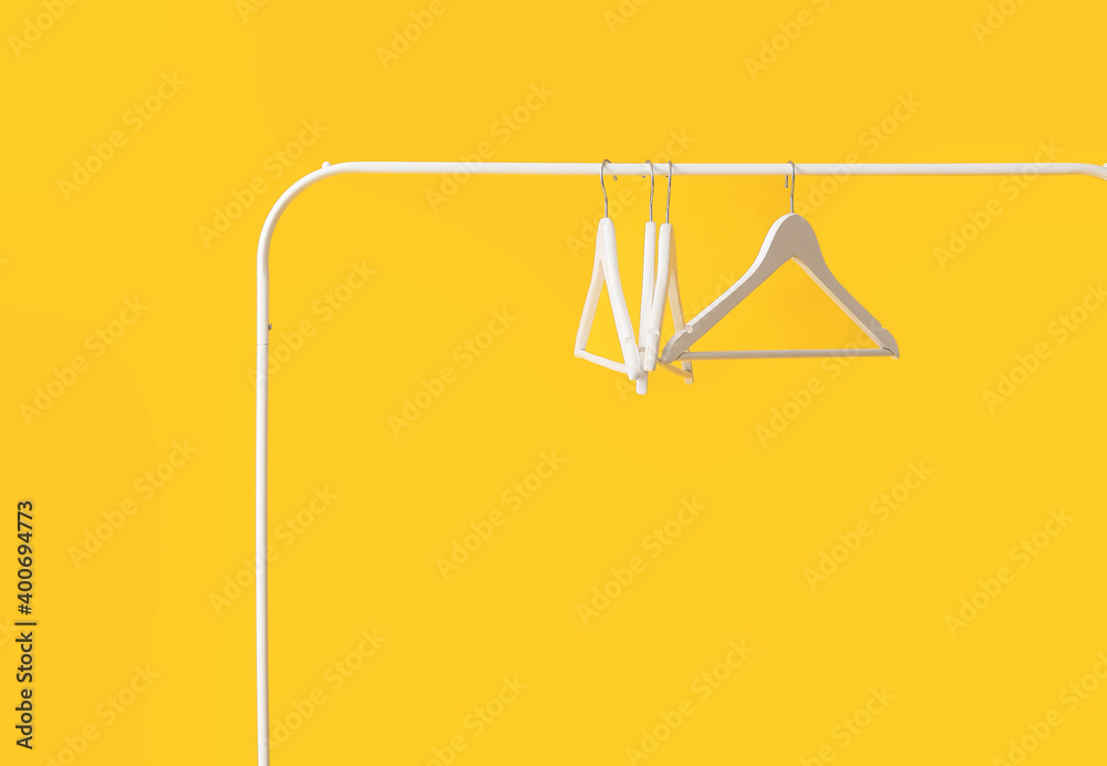 Rack with clothes hangers on color background