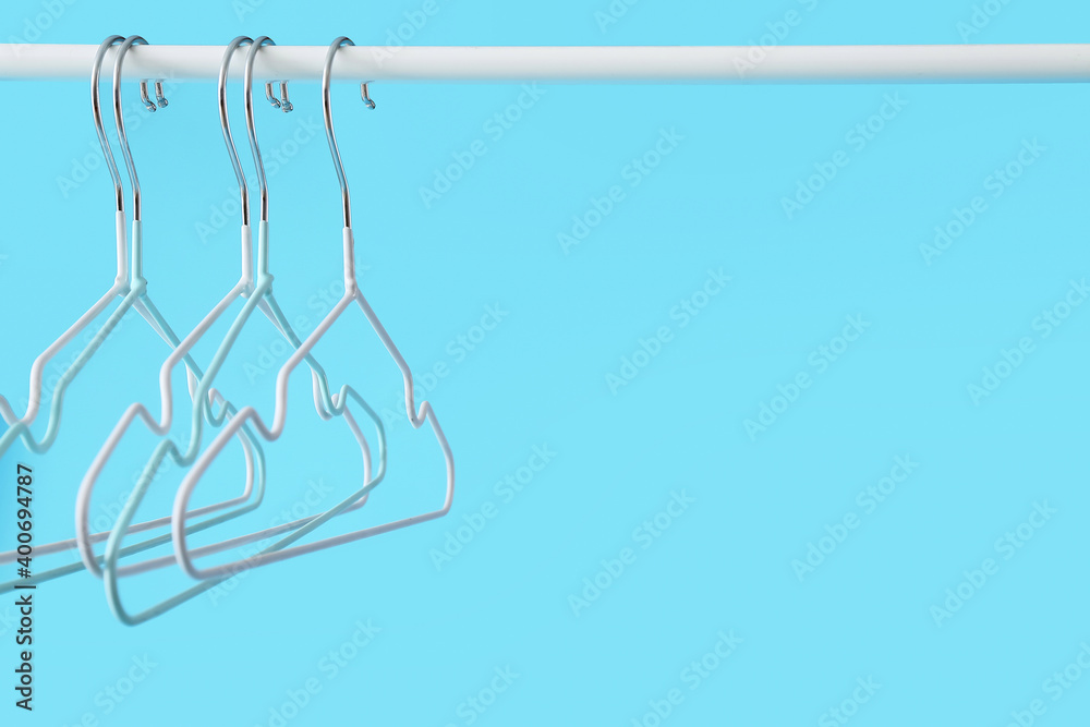 Rack with clothes hangers on color background