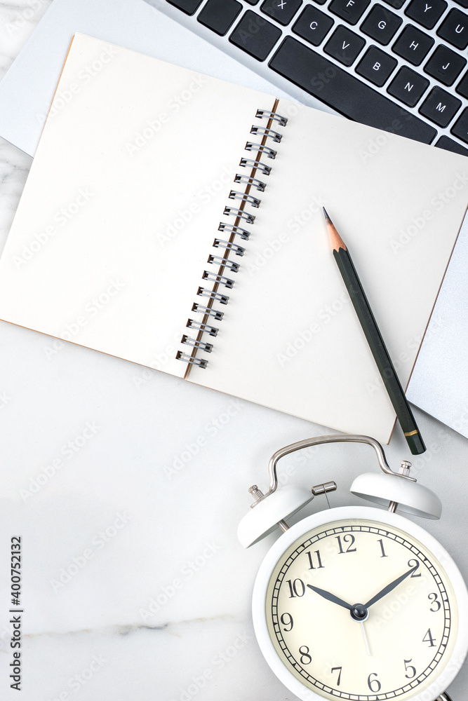 Office table desk work with blank notebook, report and alarm clock on marble white background.