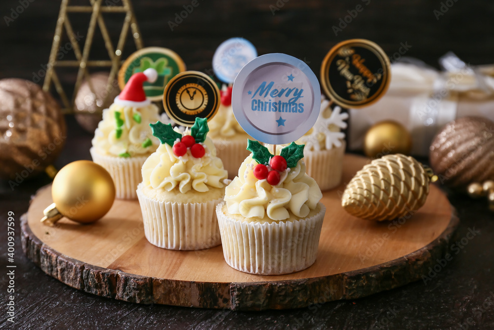 Board with tasty Christmas cupcakes on dark background