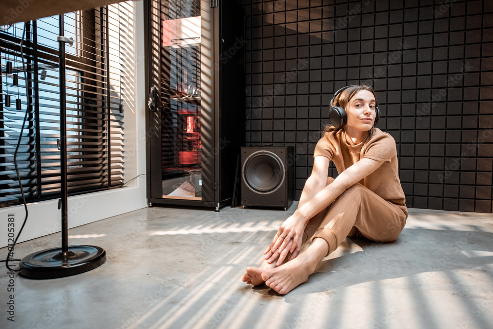 Young and cheerful woman in comfortable home suit listening to the music in headphones at the modern