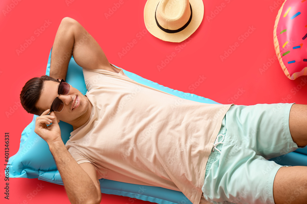 Young man lying on inflatable mattress against color background