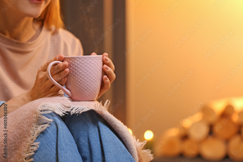 家里壁炉旁的女人正在喝茶。供暖季节的概念