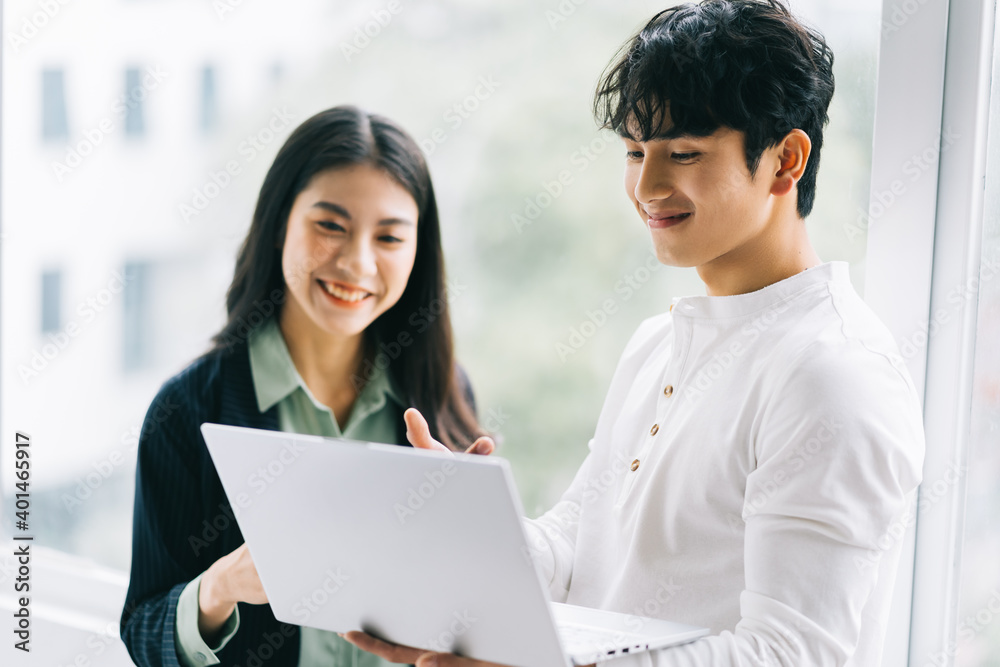 Two Asian colleagues are discussing the work. The businessman is holding a laptop in his hand