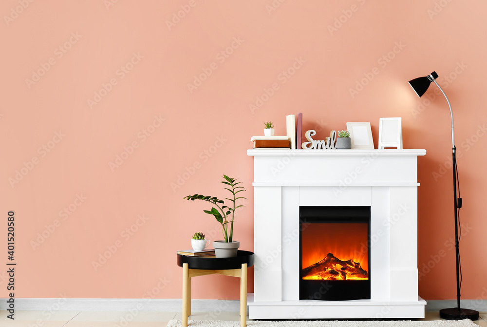 Fireplace with houseplants and lamp near color wall in room