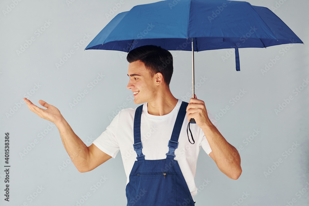 手撑雨伞。身穿蓝色制服的男工人站在工作室内，背靠白色背景