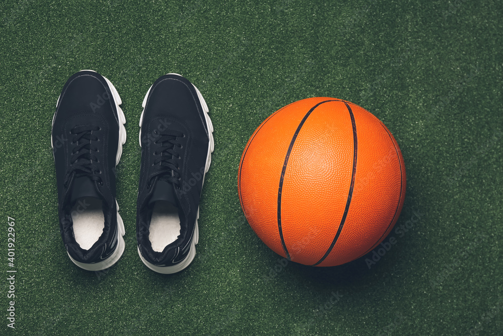 Sportive shoes and basketball on color background