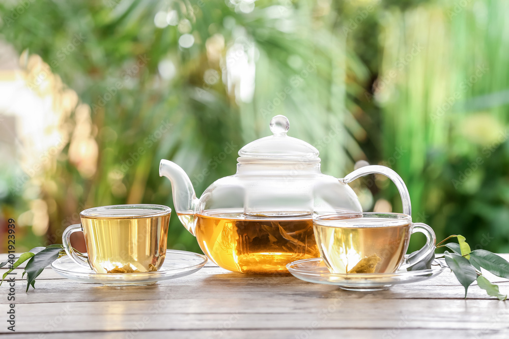 Cup of green tea and teapot on table against blurred  background