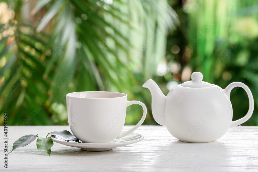 Cup of green tea and teapot on table against blurred  background