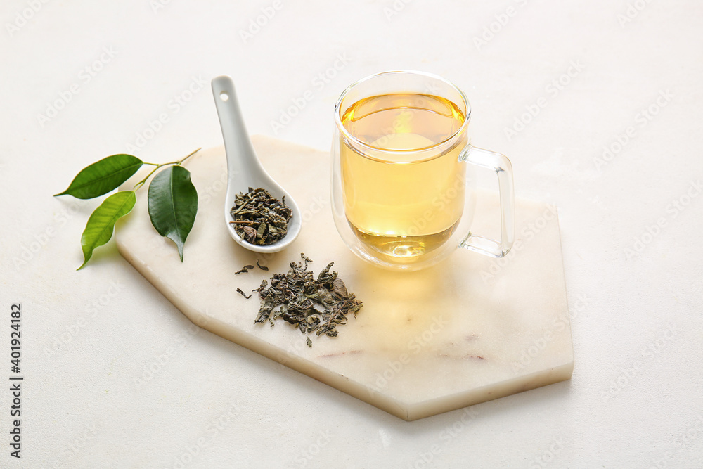 Cup of green tea and spoon with dry leaves on white background