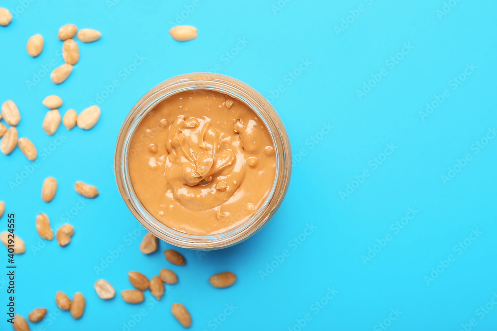 Jar with tasty peanut butter and nuts on color background