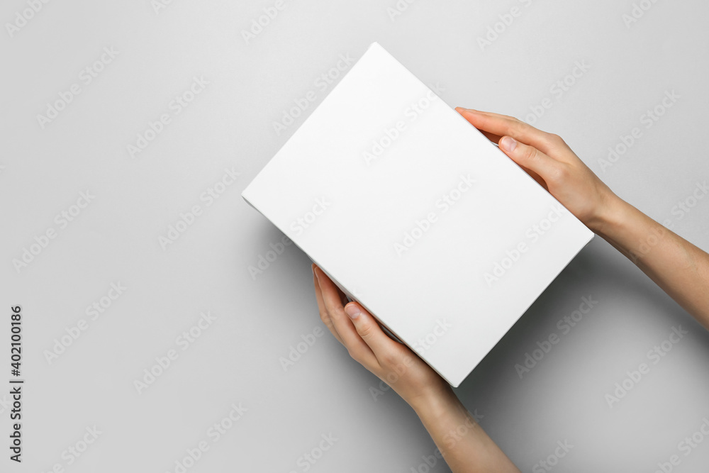 Hands with blank cardboard box on light background