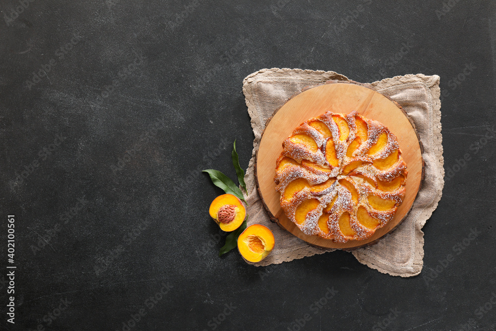 Board with tasty peach pie on dark background