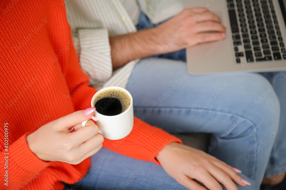 Young couple with laptop drinking hot coffee at home, closeup