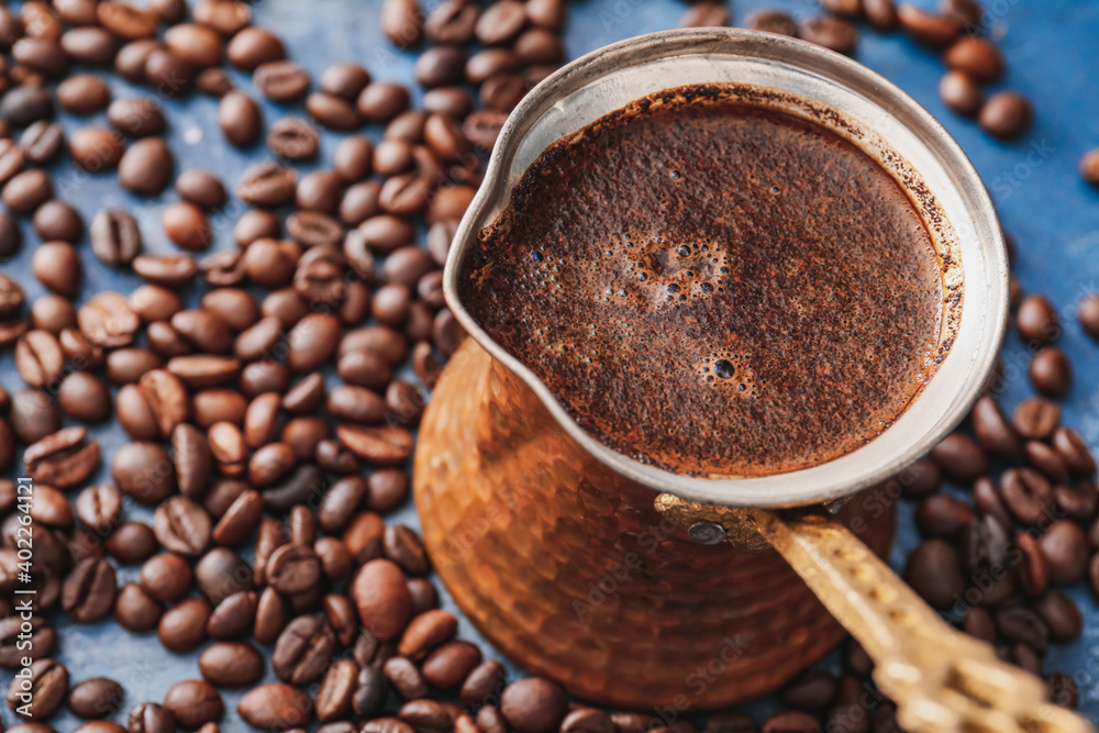 Cezve with hot coffee and beans on table