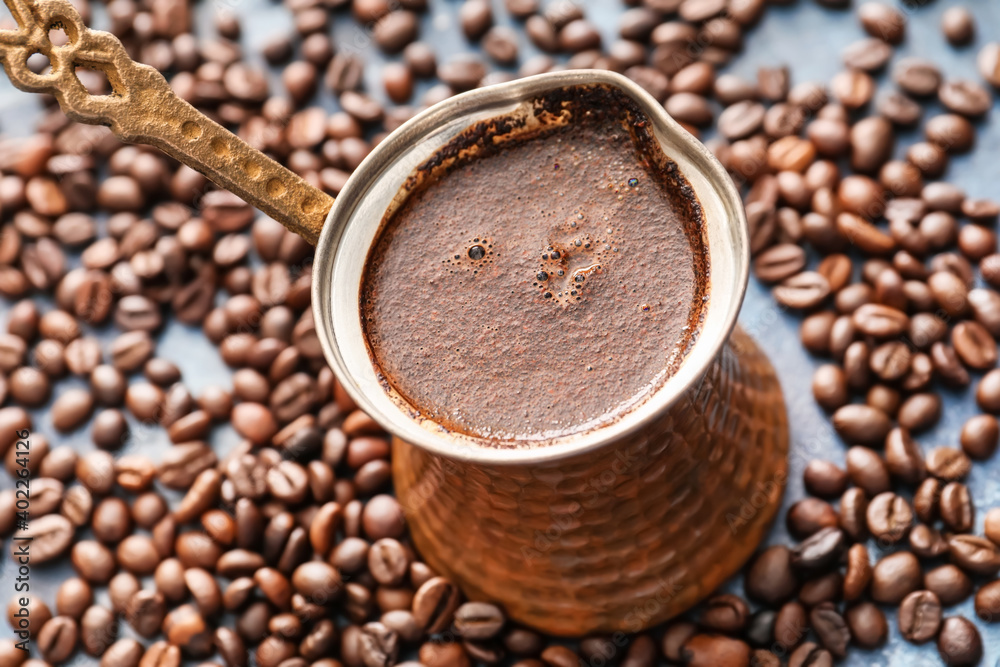 Cezve with hot coffee and beans on table