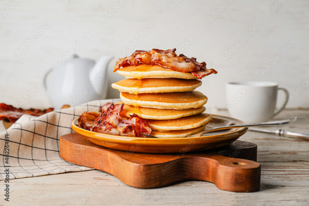 Plate with tasty pancakes and fried bacon on wooden table