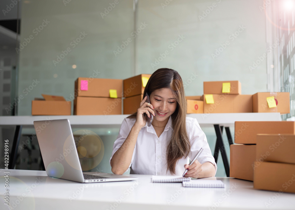 Young Asian entrepreneur owner talking on phone at workplace at home. Start up small business.