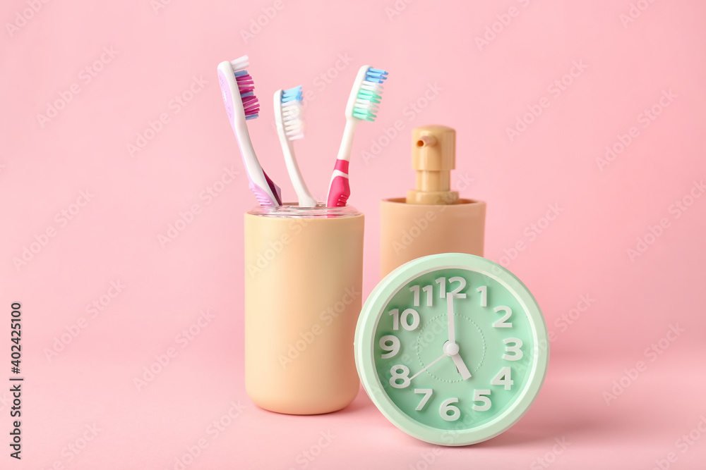 Alarm clock, soap and toothbrushes on color background