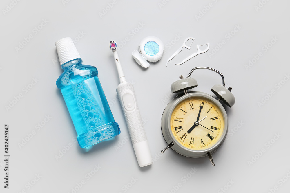 Set of oral care products and alarm clock on grey background