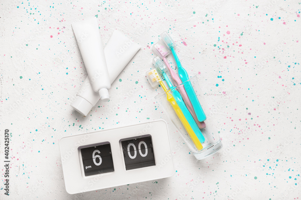 Alarm clock, paste and toothbrushes on light background