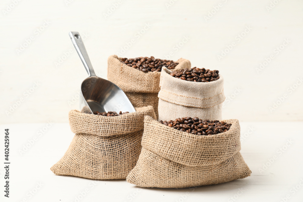 Bags with coffee beans and scoop on white background