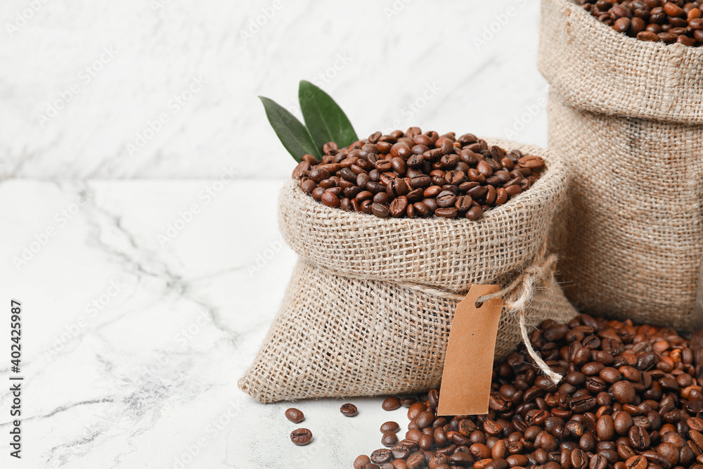 Bags with coffee beans on light background