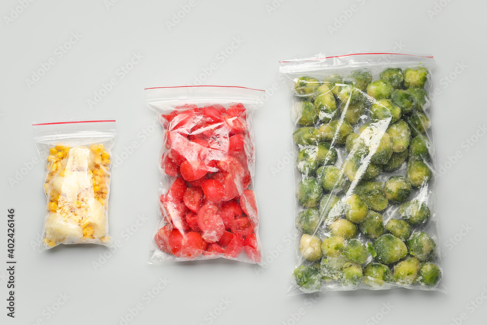 Plastic bags with frozen vegetables on light background