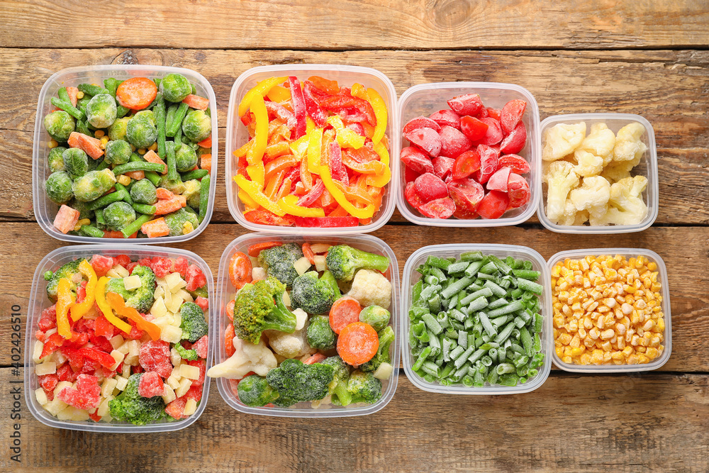 Plastic containers with frozen vegetables on wooden background