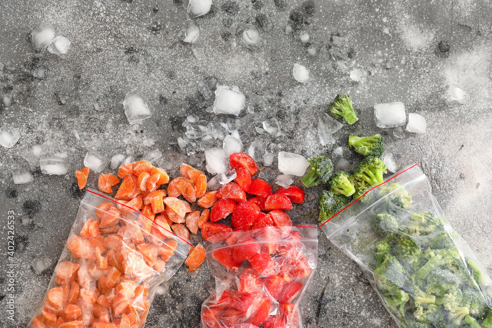 Plastic bags with frozen vegetables and ice on dark background