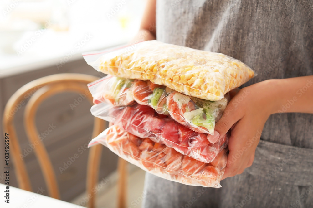 Woman holding bags with frozen vegetables in kitchen