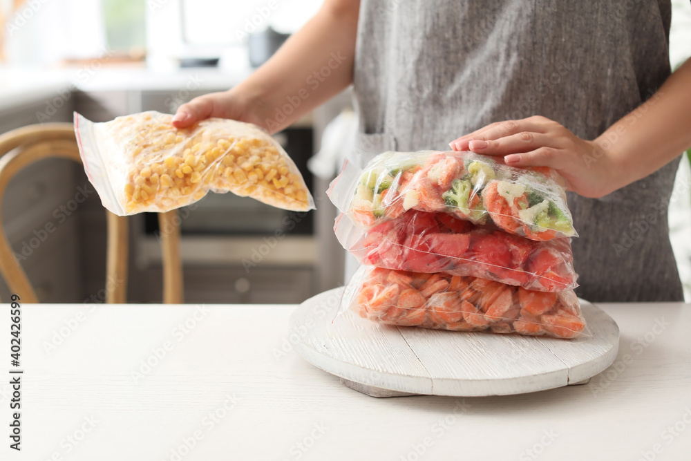 Woman holding bags with frozen vegetables in kitchen