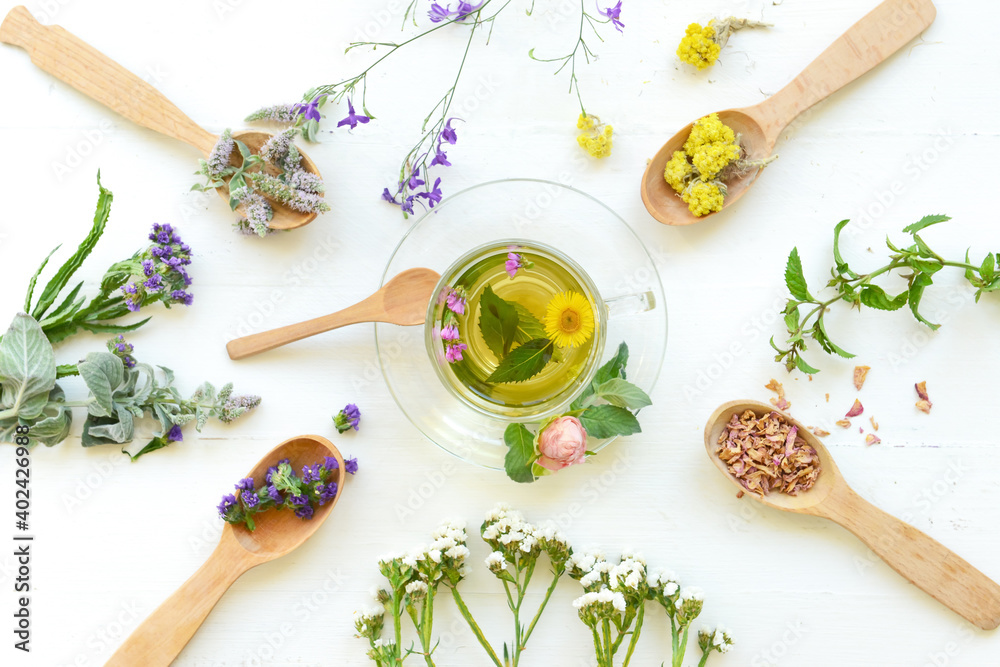 Flowers, spoons and cup with floral tea on light background