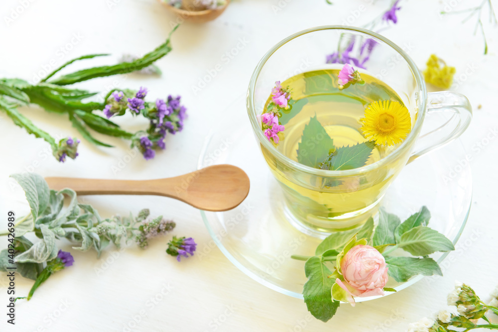 Flowers, spoon and cup with floral tea on light background