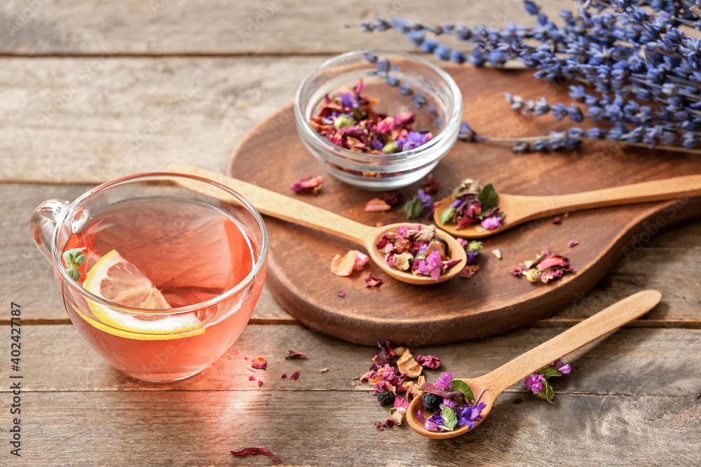 Cup with floral tea and dry flowers in spoons on wooden background